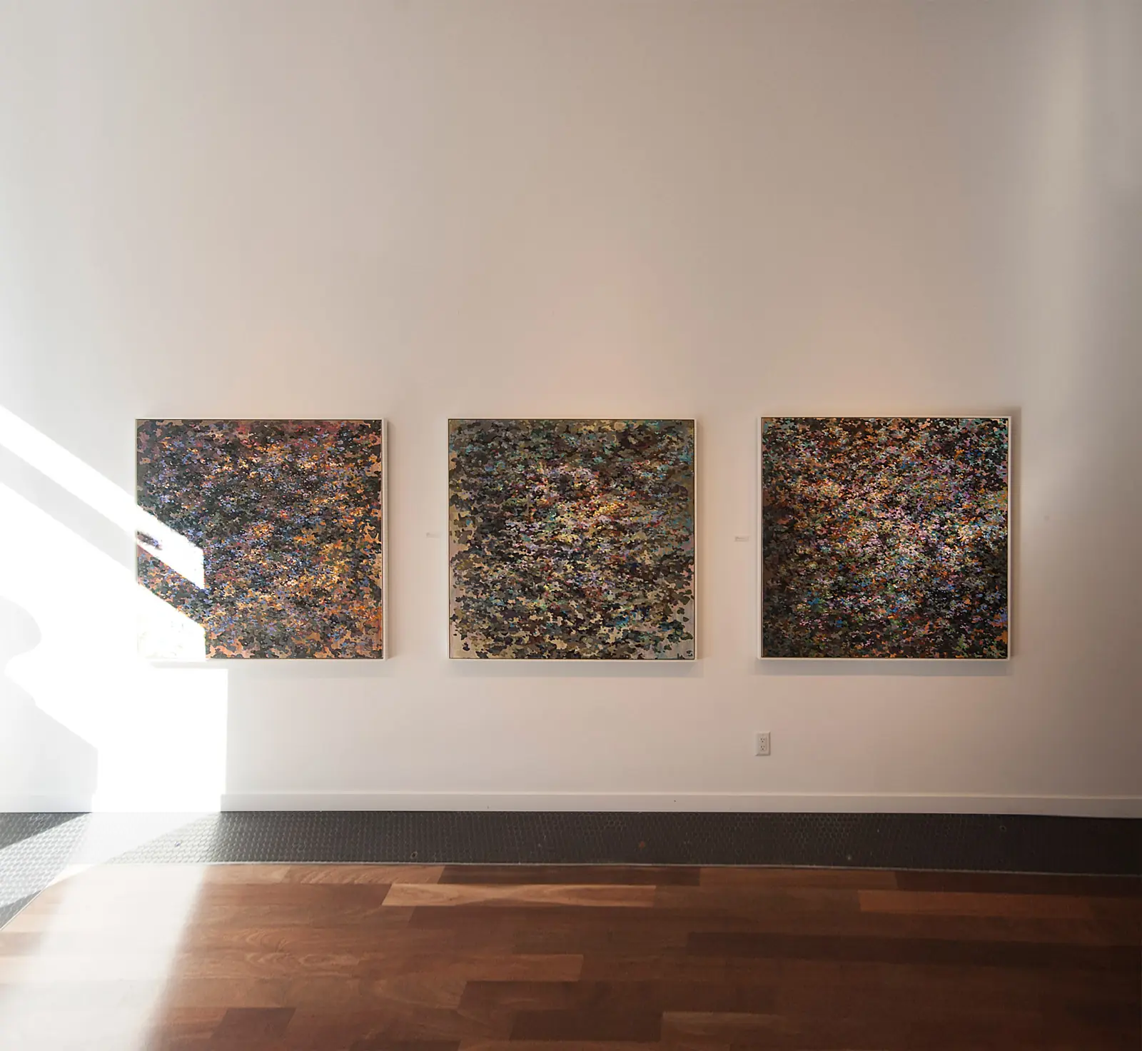 Three paintings installed in a sunlit gallery