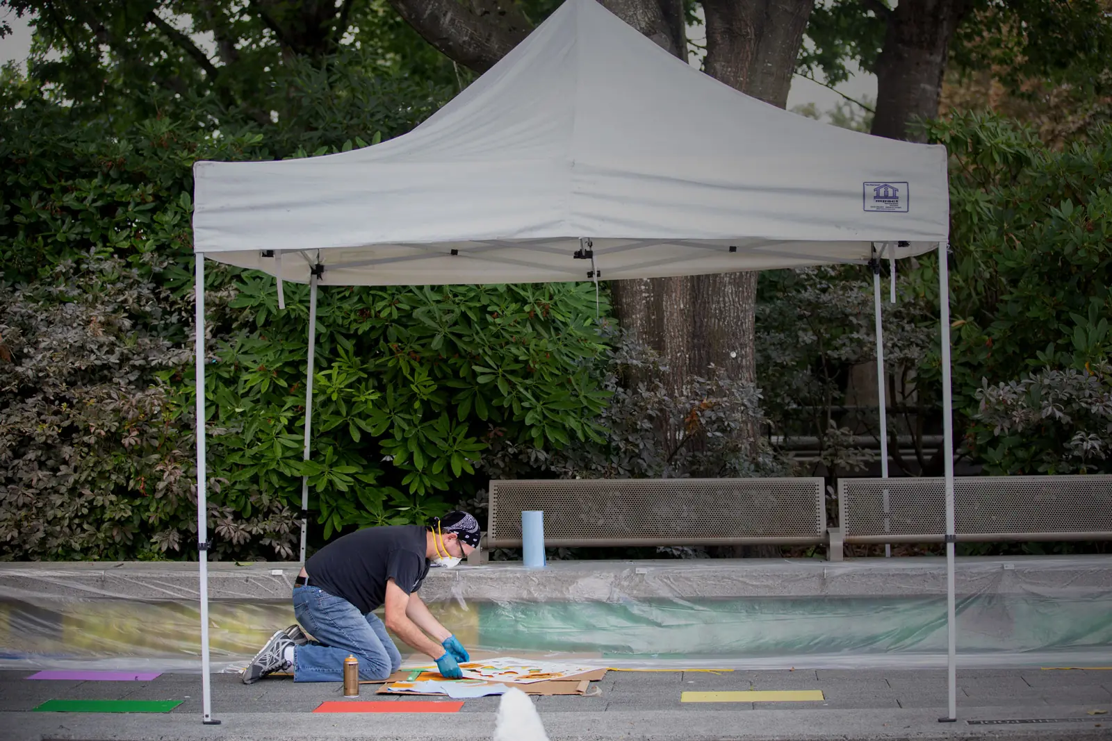 Artist painting colour onto the ground beneath a white canopy