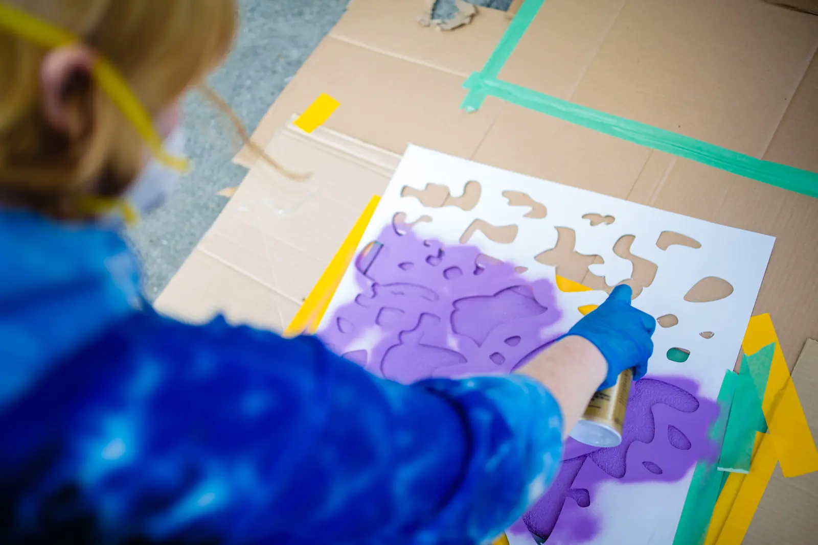 Gloved hands painting purple forms onto a prepared surface
