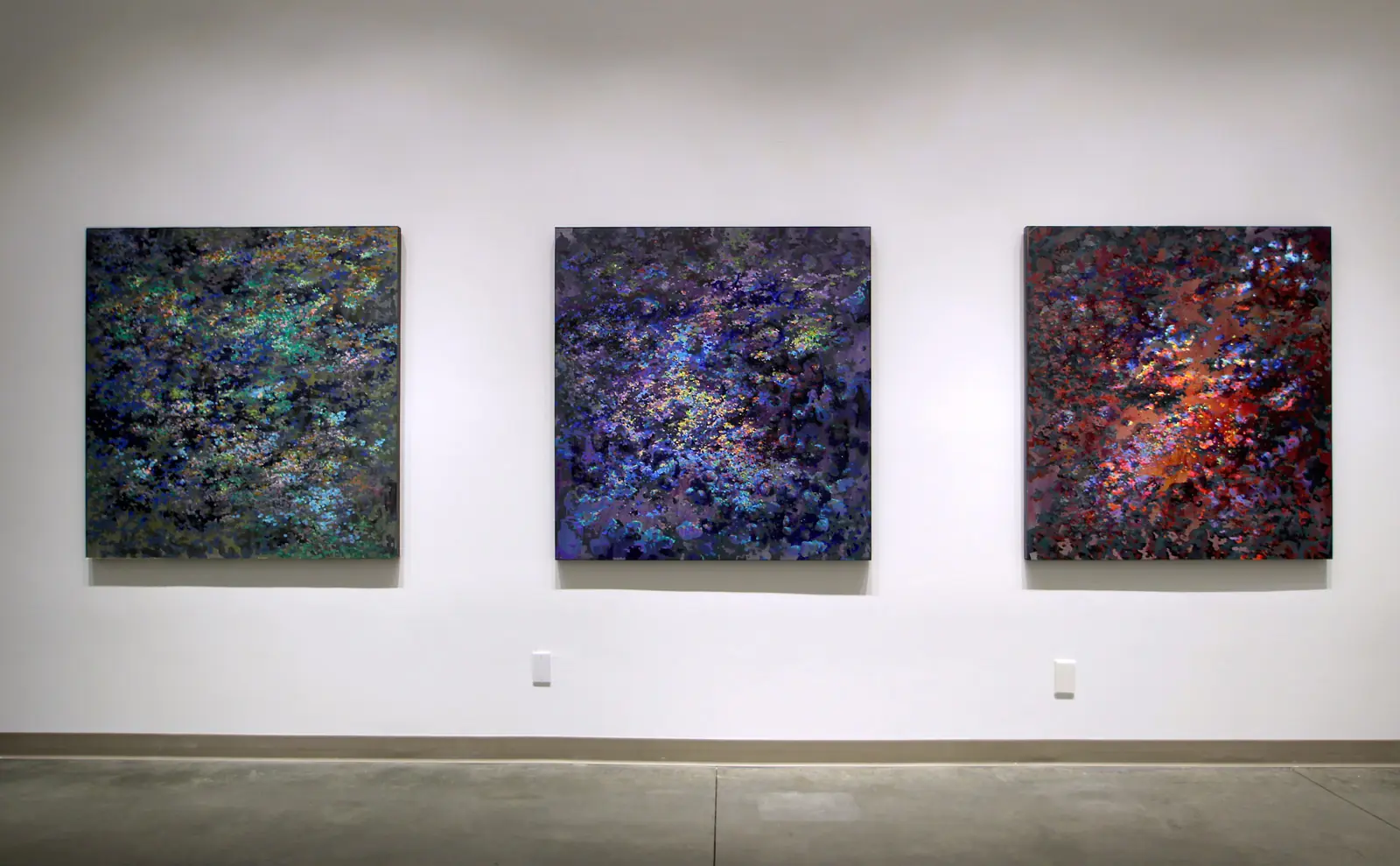 Three abstract paintings displayed together on a white wall